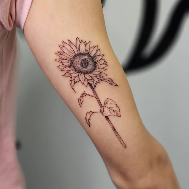 Tatuaje de girasol en la parte interior del antebrazo de una persona sobre un fondo claro.
