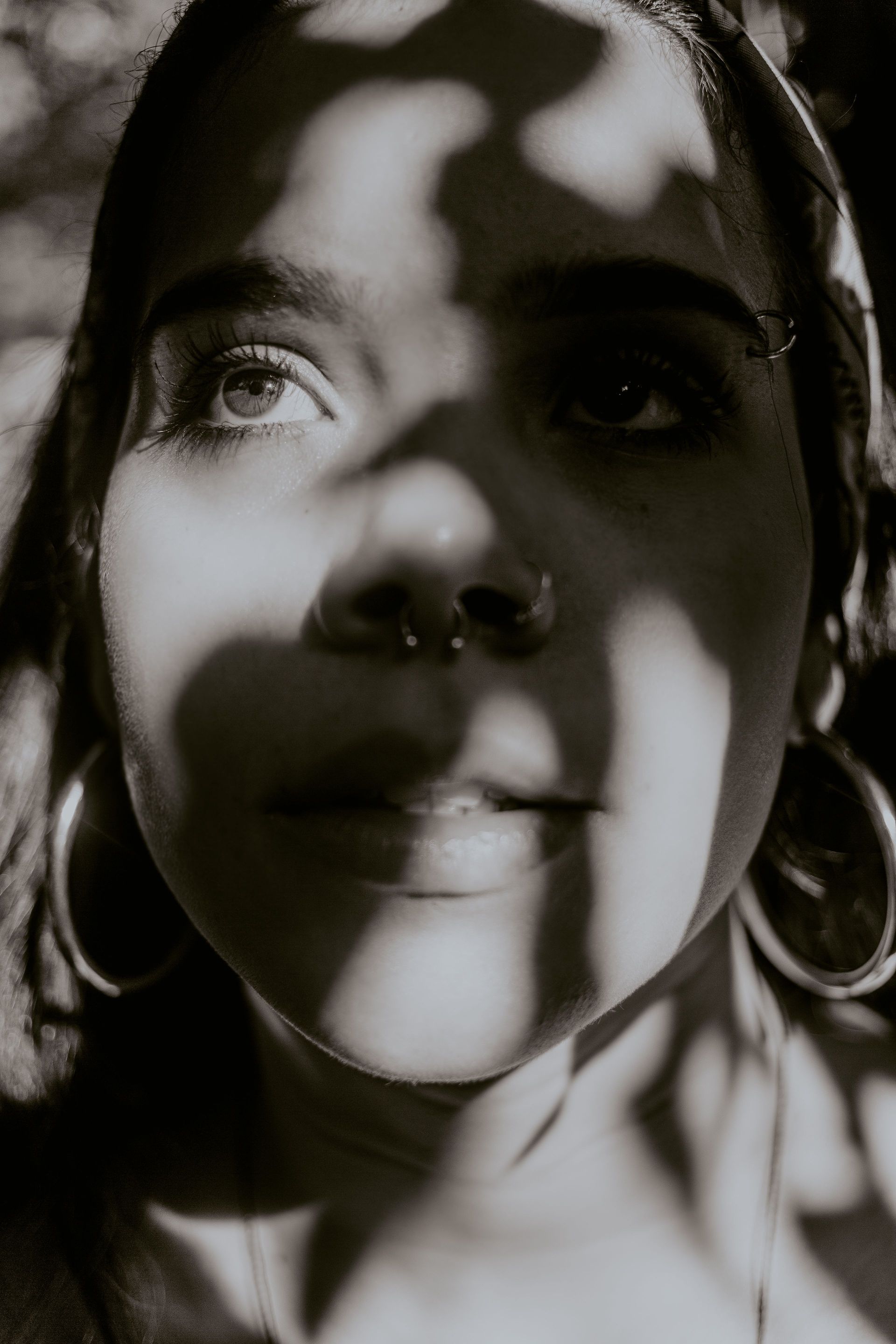 Retrato en blanco y negro de primer plano de una persona con luz tamizada sobre su rostro, que lleva pendientes de aro.