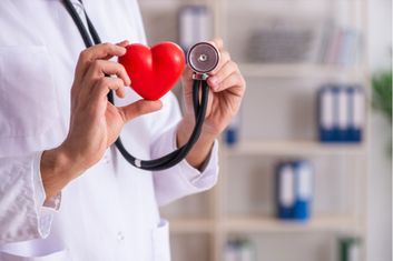 Person hält rotes Herz in der einen und Stethoskop in der anderen Hand