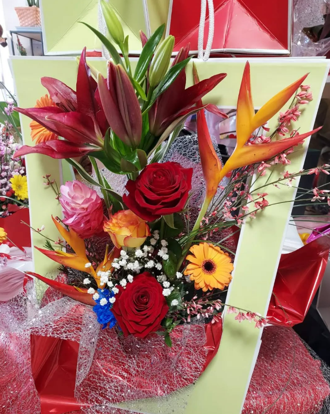 Composition florale colorée dans un cadre vert citron, comprenant des lys, des roses et des fleurs d'oiseau de paradis.