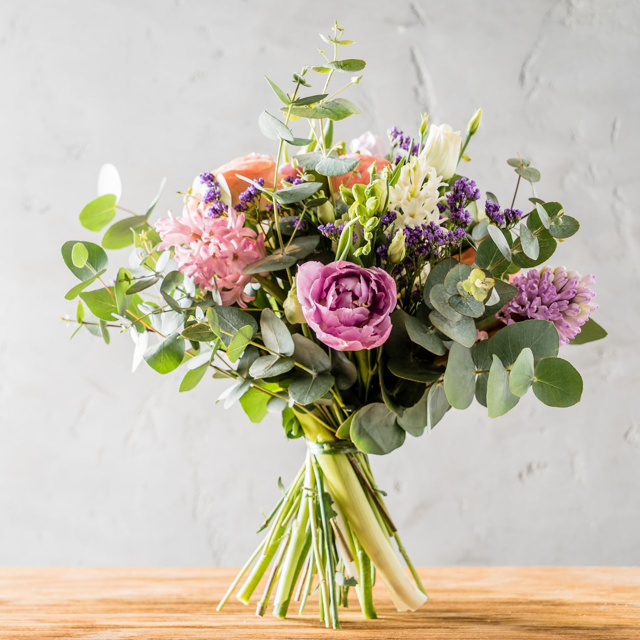 Bouquet de fleurs roses, violettes et blanches avec de l'eucalyptus vert, attaché avec des tiges vertes, sur une table en bois.