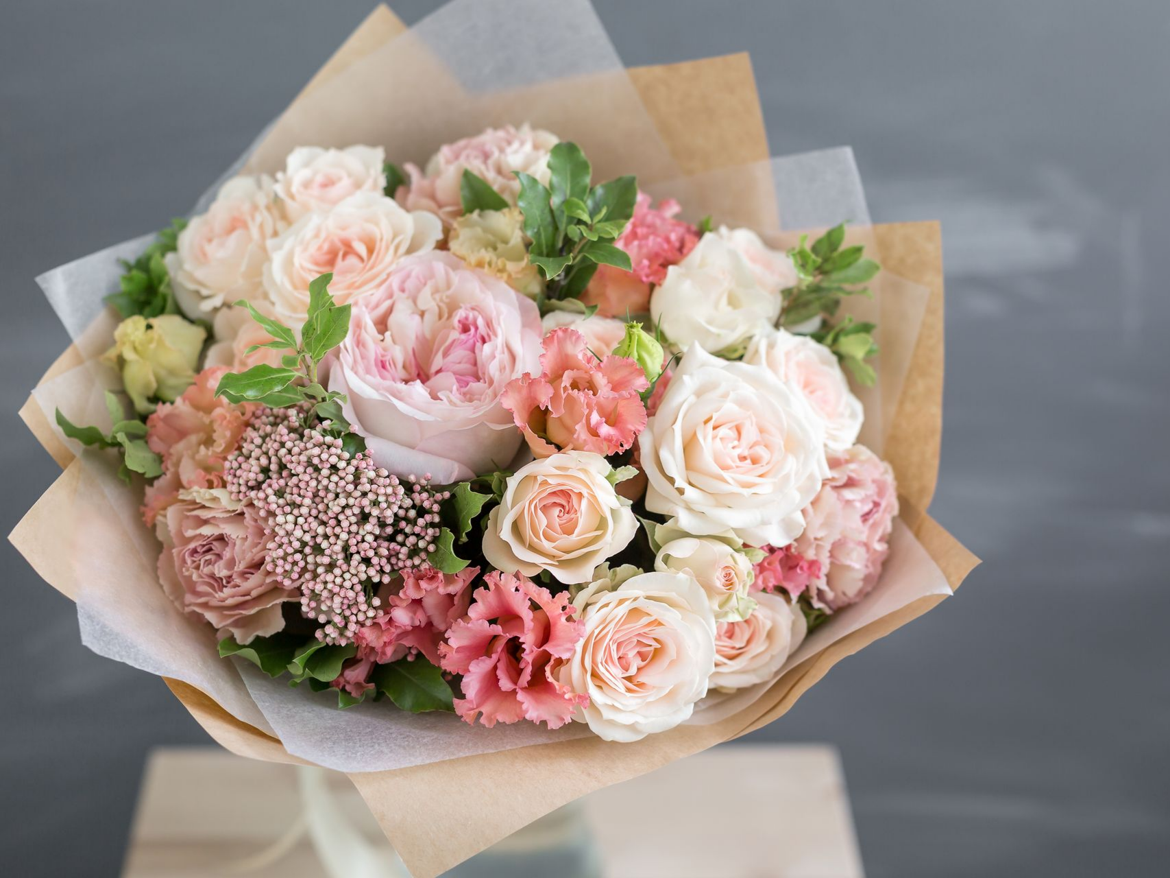 Bouquet de roses rose clair et pêche et d'œillets emballés dans du papier brun.