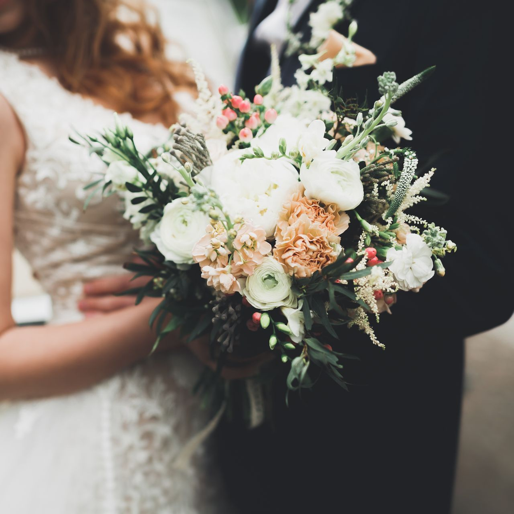 Mariés avec un bouquet de fleurs crème, pêche et vertes ; photo de détail.