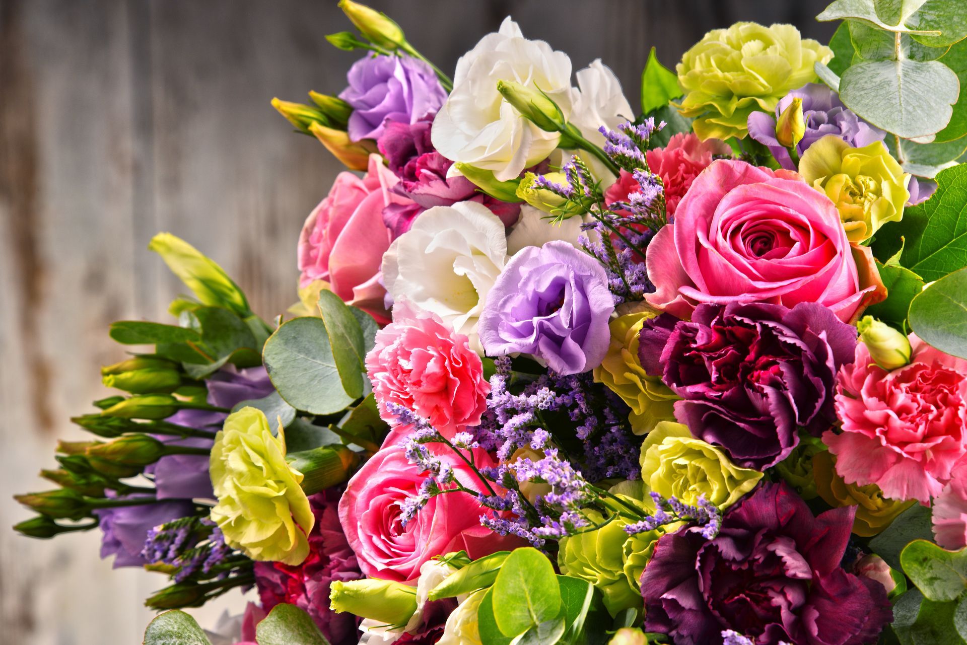 Bouquet vibrant de fleurs roses, violettes, blanches et jaunes avec un feuillage vert sur un fond de bois.