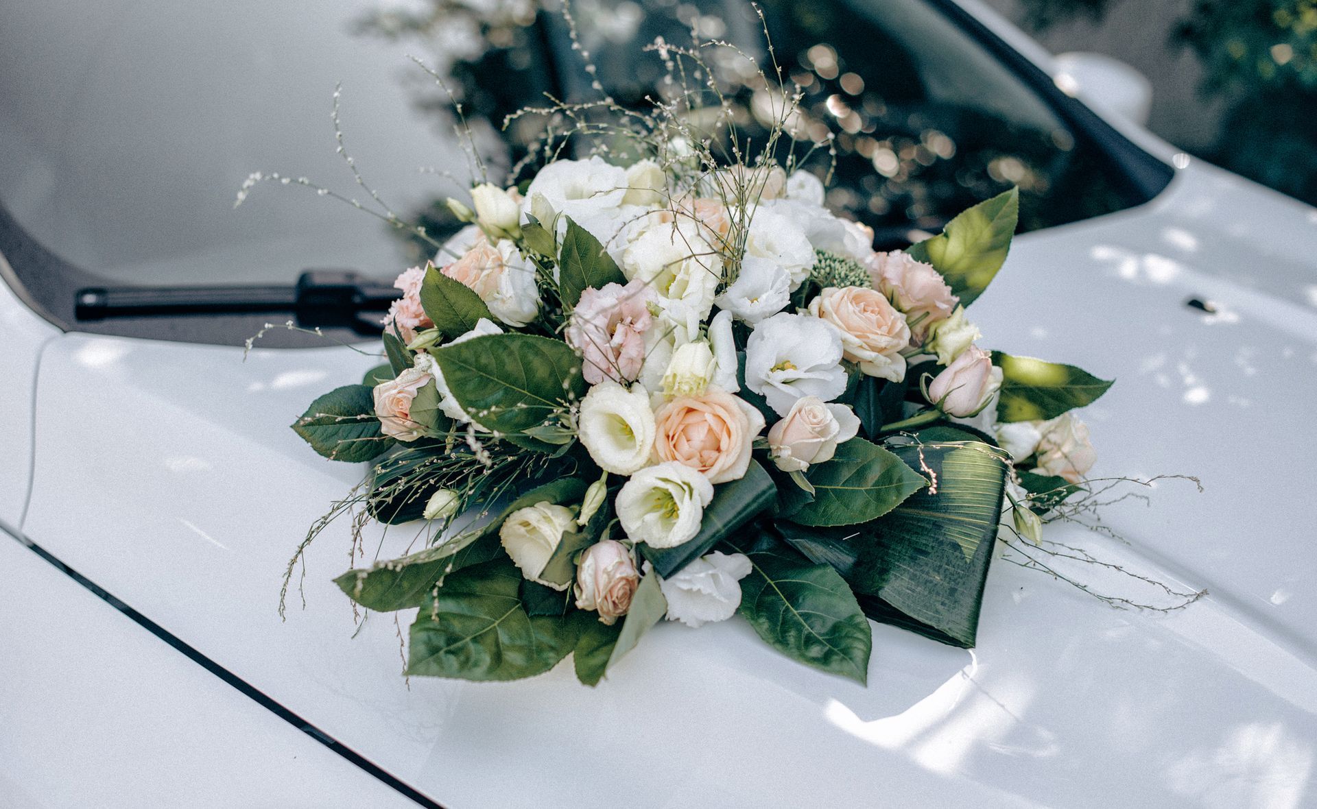 Bouquet de mariage de roses crème et pêche sur un capot de voiture blanc.