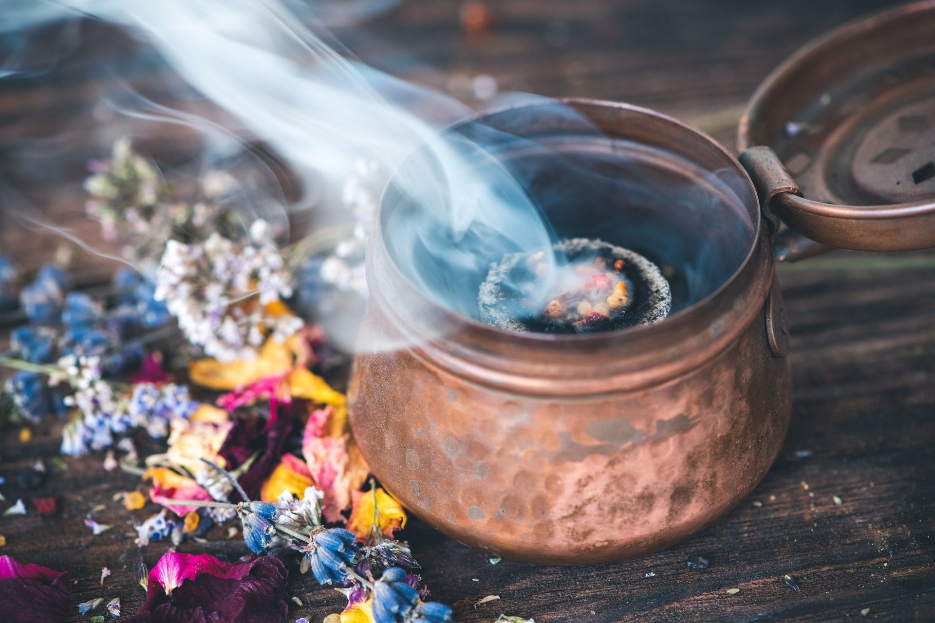 Brûle-encens en cuivre émettant de la fumée, entouré de fleurs et de pétales sur bois.