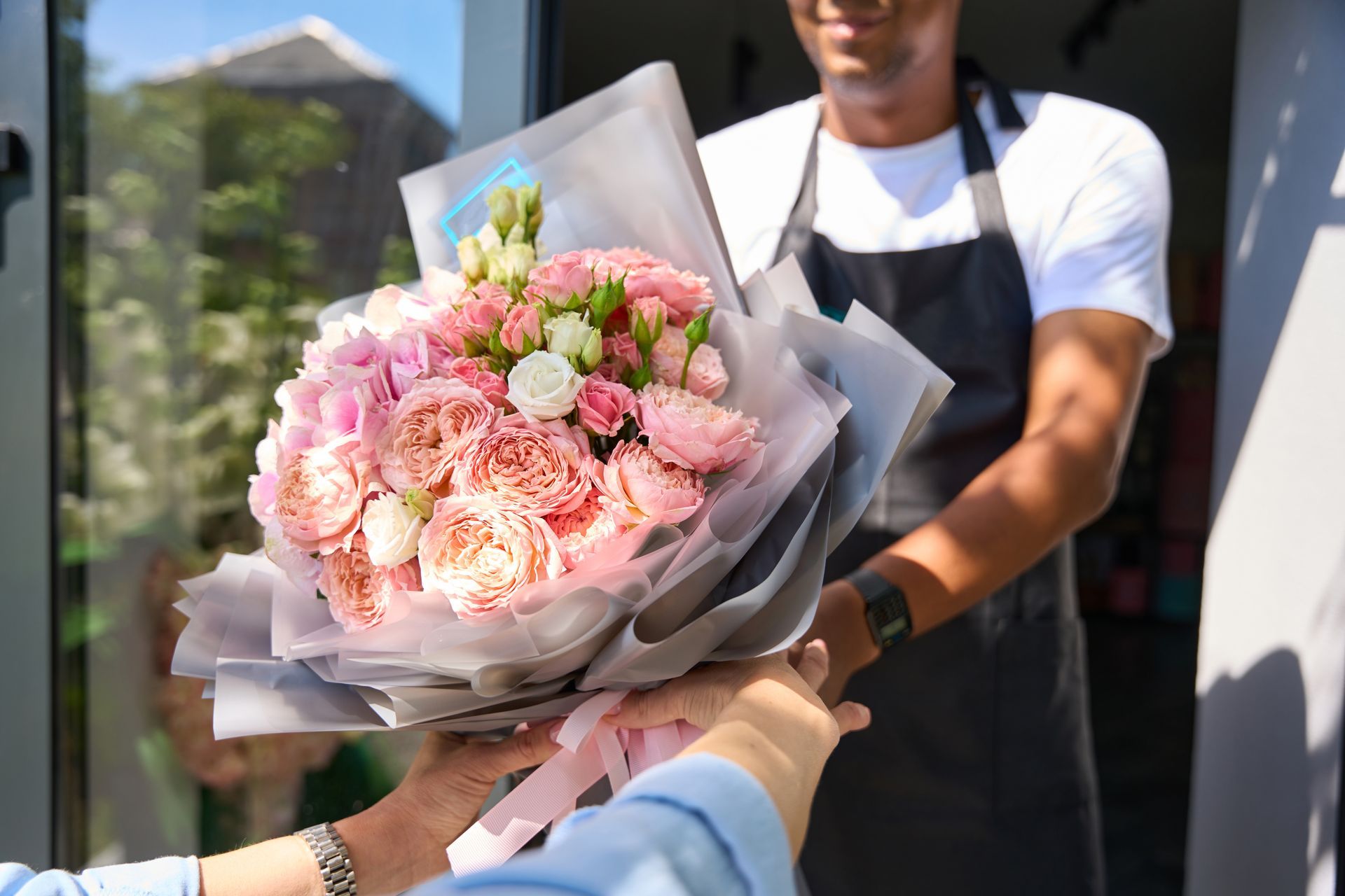 Un homme en tablier livrant un bouquet de fleurs roses à une personne à l'extérieur d'un bâtiment.