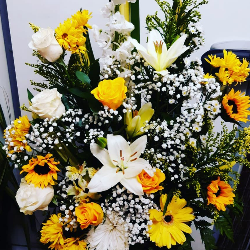 Composition florale : tournesols jaunes, lys et roses blancs, gypsophile et verdure.