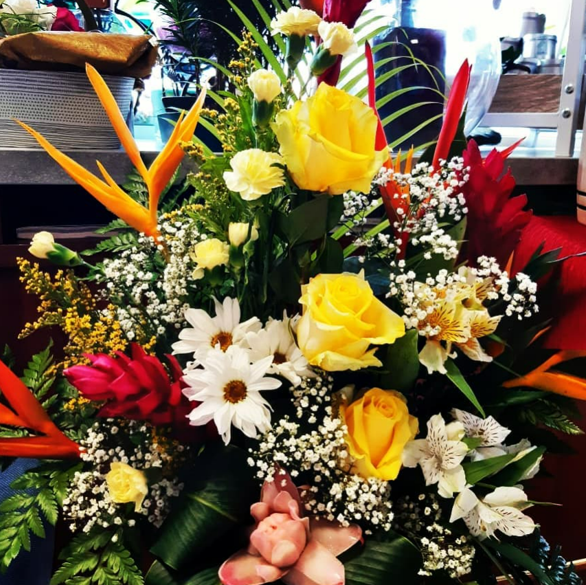 Composition florale tropicale colorée avec des roses jaunes, des marguerites blanches et du gingembre rouge.