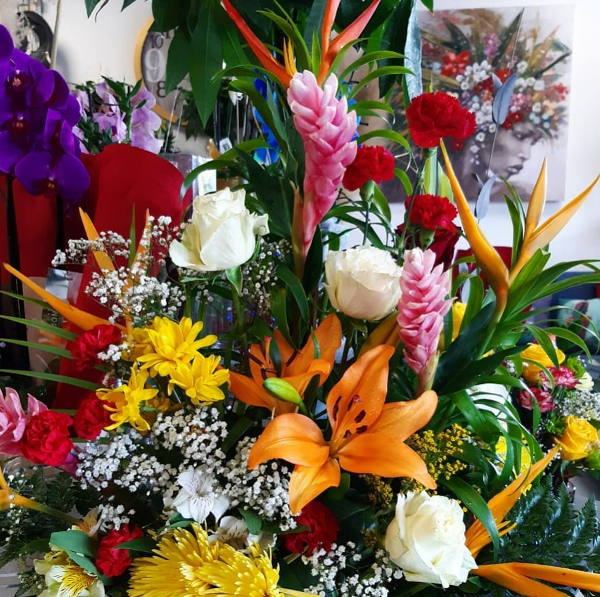 Composition florale colorée avec des lys orange, des roses blanches et des fleurs tropicales.