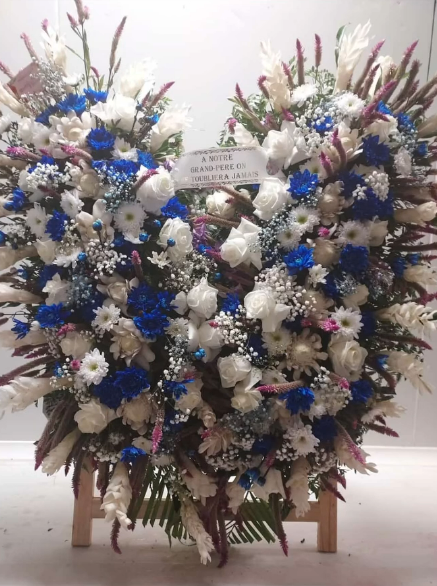 Composition florale en forme de cœur composée de fleurs bleues, blanches et autres sur un support en bois.