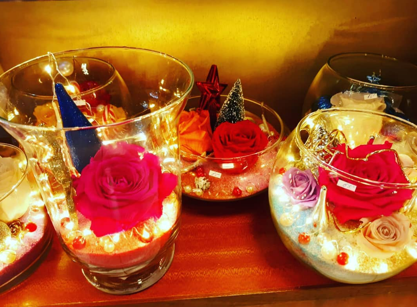 Vases en verre avec des roses préservées et des lumières exposées sur une étagère.
