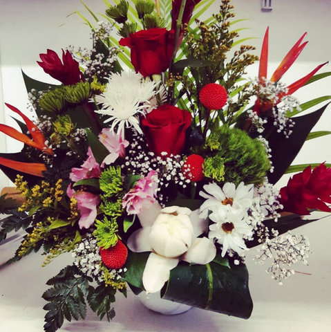 Composition florale avec des roses rouges, des marguerites blanches et de la verdure dans un vase blanc.