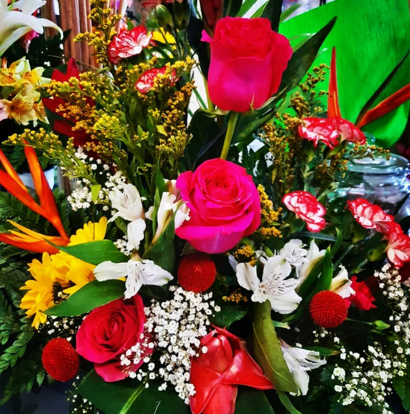 Gros plan d'une composition florale vibrante composée de roses roses, de tournesols jaunes et de diverses autres fleurs colorées.