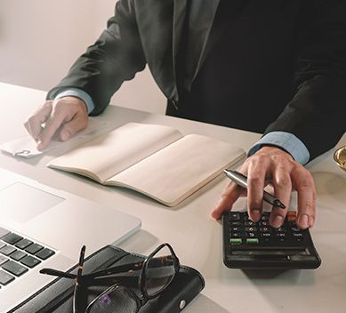 Un hombre está sentado en un escritorio usando una calculadora y escribiendo en un cuaderno.