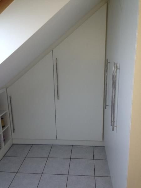 Ein Raum mit Dachschräge und weißen Schränken.