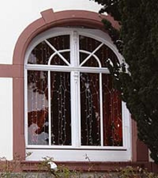 Ein großes Bogenfenster an der Seite eines Gebäudes mit einem Baum im Hintergrund.