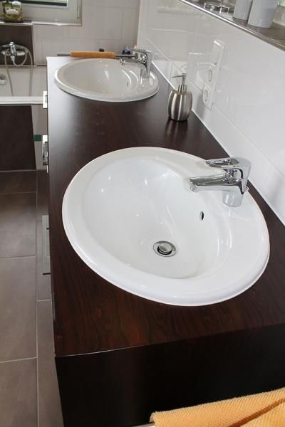 Zwei weiße Waschbecken auf einer Holzablage in einem Badezimmer