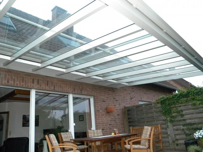 Eine Terrasse mit Tisch und Stühlen unter einem Glasdach