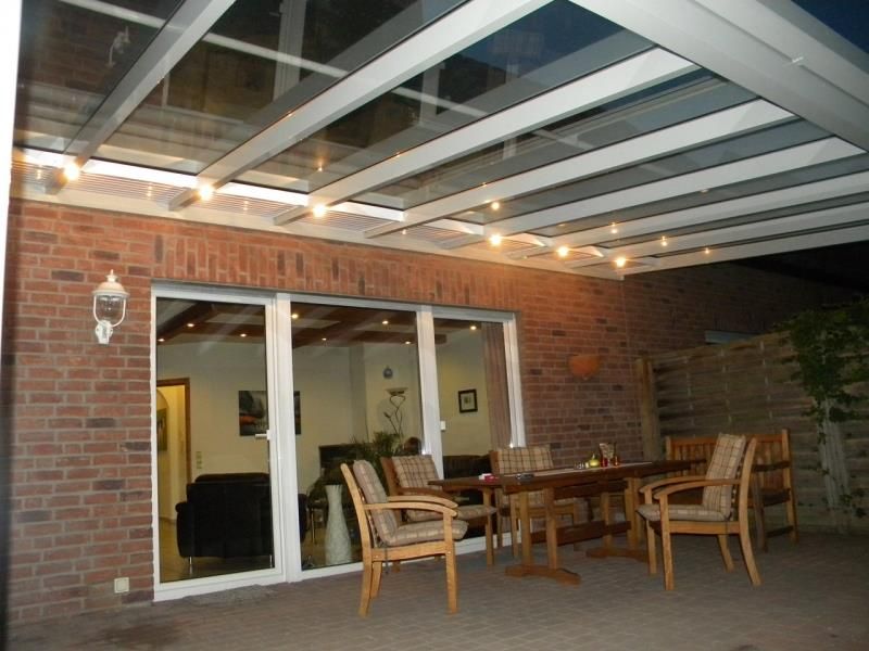 Eine Terrasse mit Tisch und Stühlen unter einem Glasdach