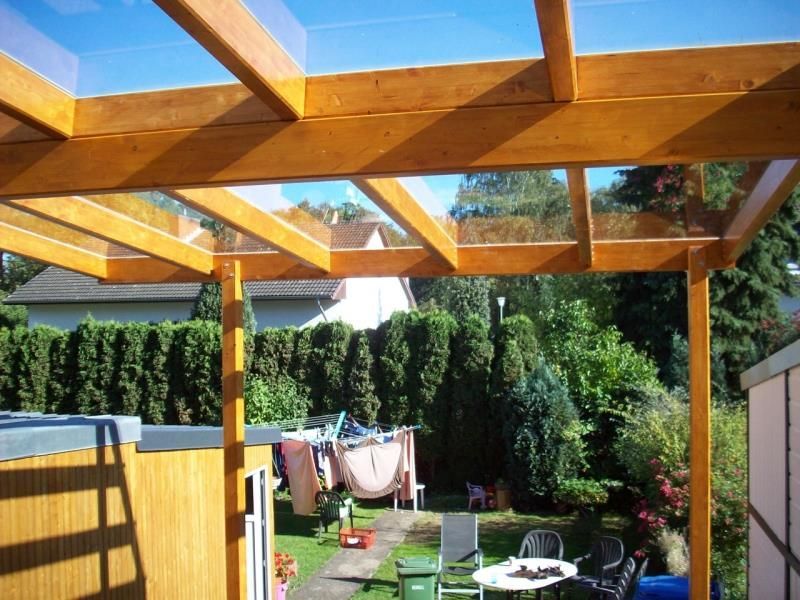 Eine hölzerne Pergola mit Glasdach mit Blick auf einen Garten