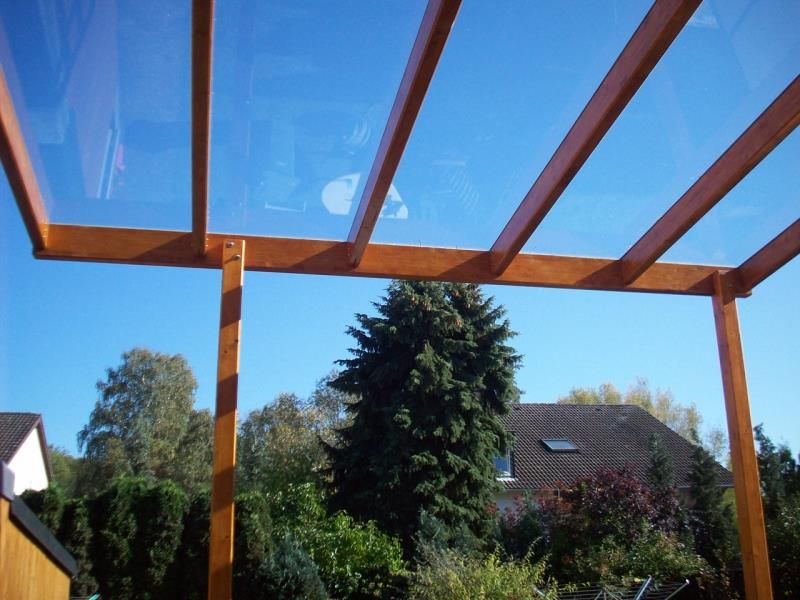 Eine Pergola mit klarem Glasdach und einem Haus im Hintergrund