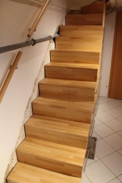 Eine Holztreppe mit Metallgeländer führt zu einem gefliesten Boden hinauf.