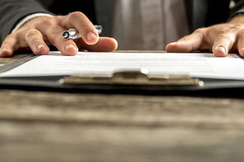 Un hombre está firmando un documento en un portapapeles con un bolígrafo.