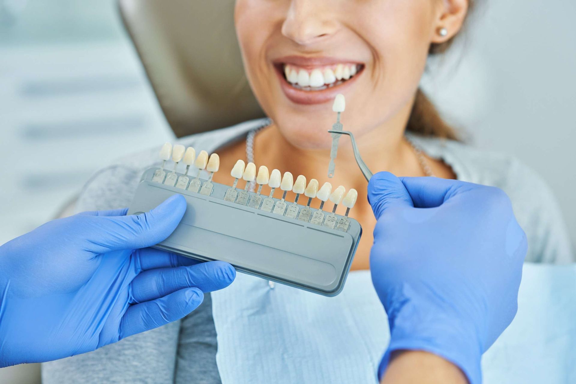 Un dentista sostiene una tabla de colores de dientes frente a la boca de una mujer.