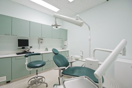 Un consultorio dental vacío con una silla verde y una computadora.