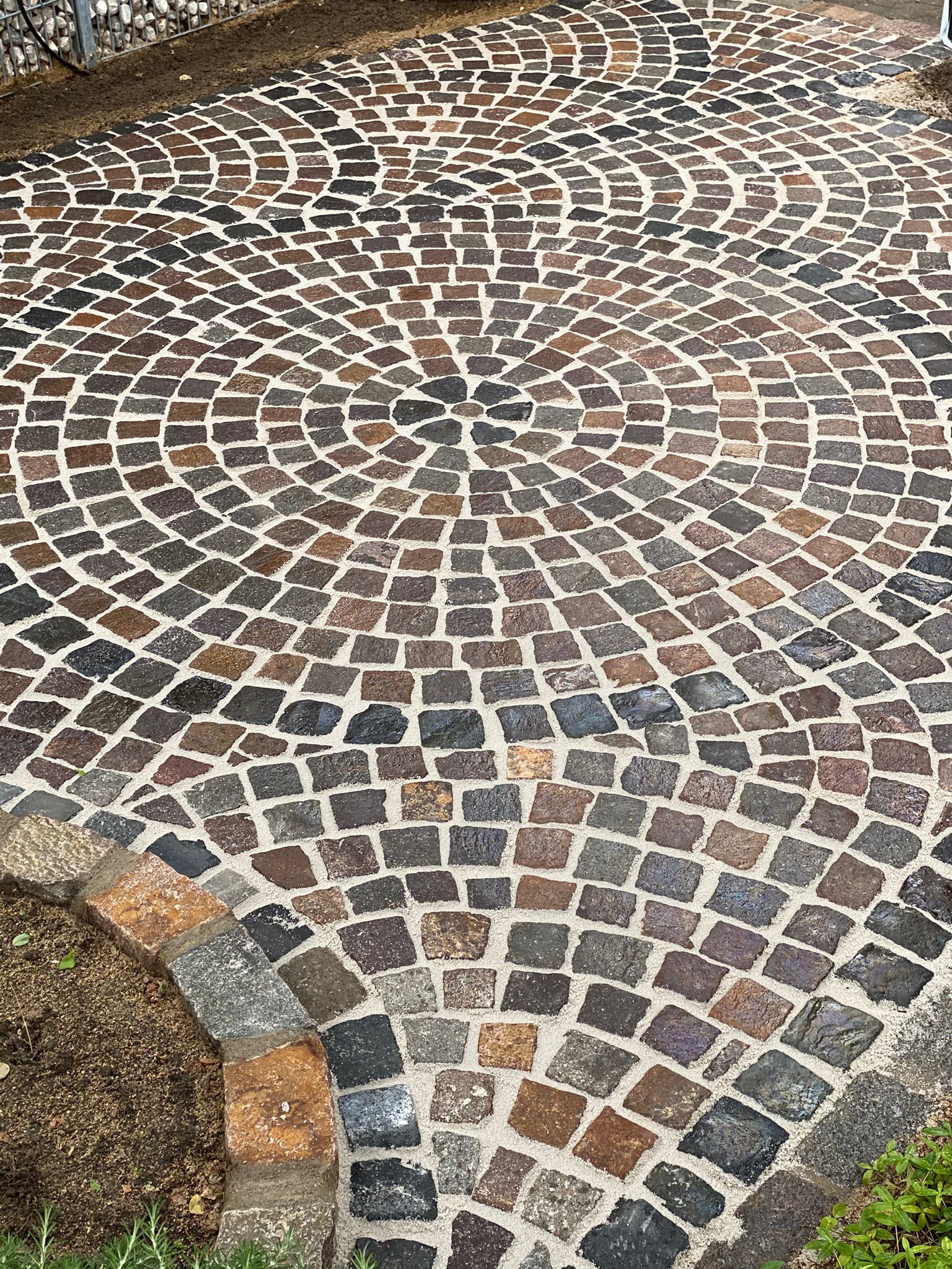 Runder, mit Kopfsteinpflaster belegter Patio aus braunen, grauen und hellbraunen Steinen.