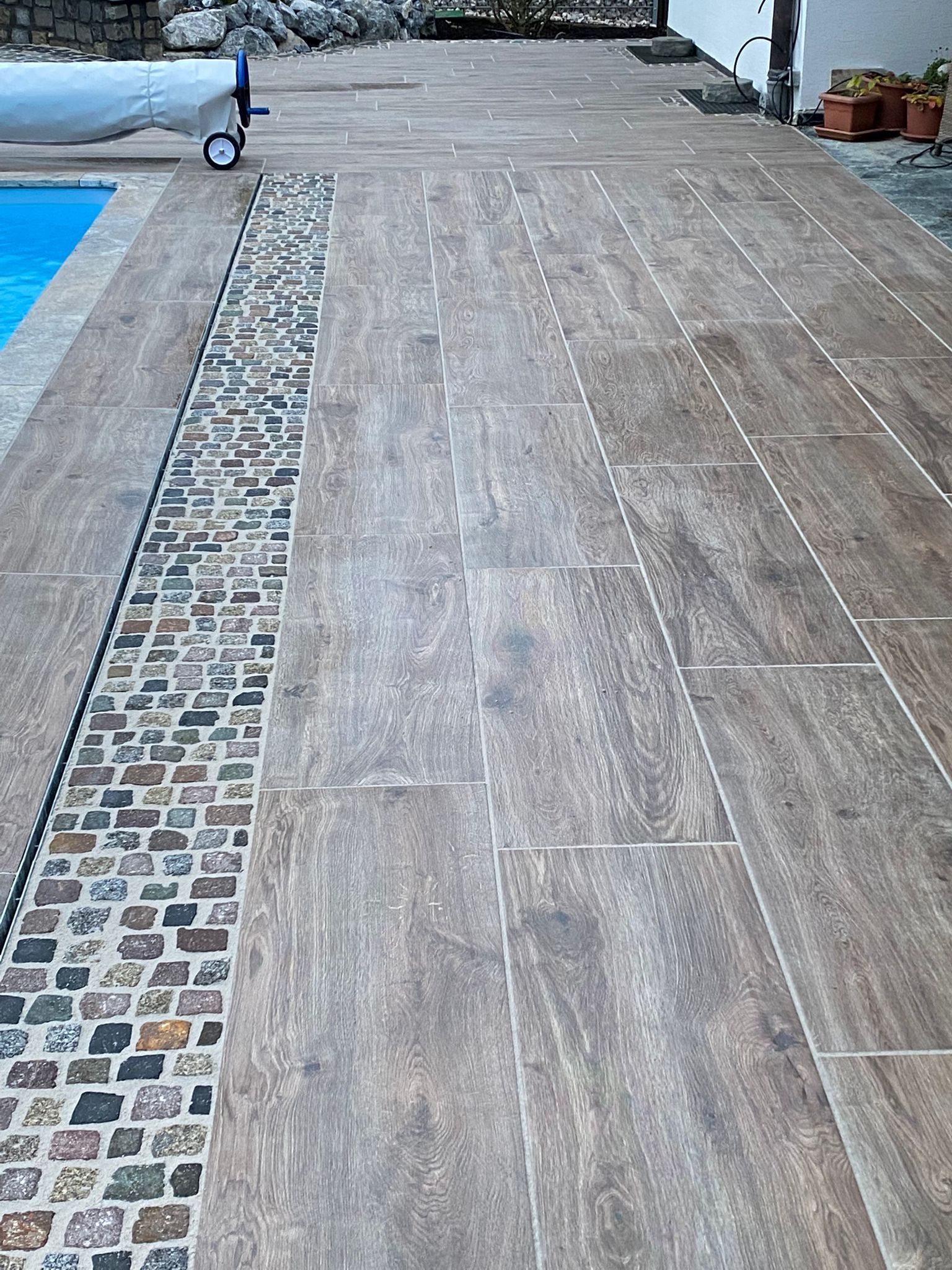Terrasse am Pool mit Stein- und Holzoptikfliesen, inklusive Mosaikablauf.