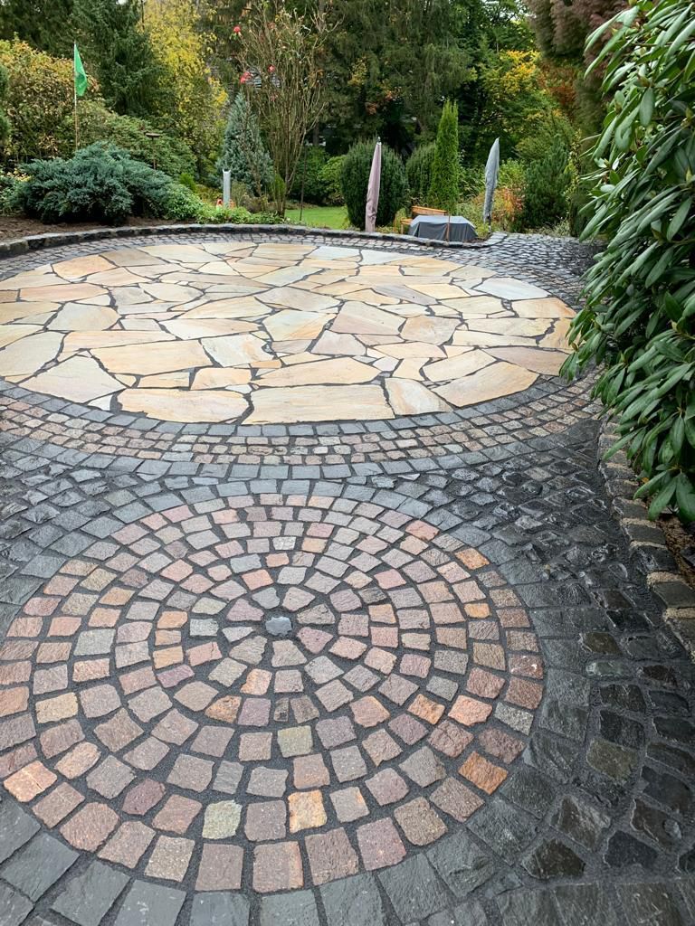 Eine Steinterrasse mit kreisförmigem Muster führt zu einem Plattenweg im Garten.