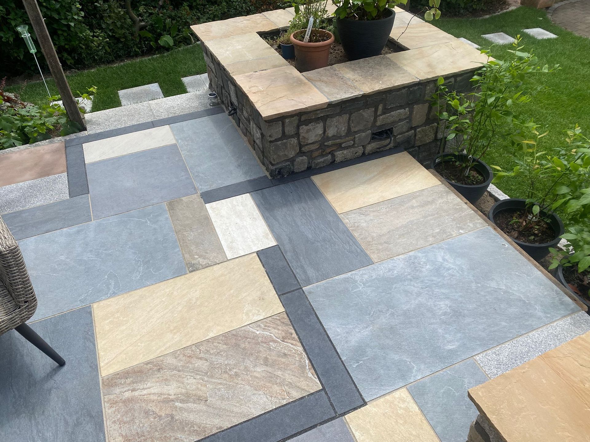 Terrasse mit Steinplatten, Feuerstelle und Topfpflanzen.