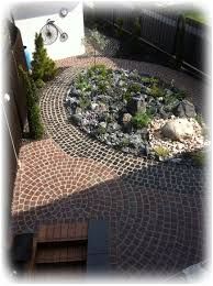 Ein geschwungener Backsteinweg umgibt einen Steingarten und einen kleinen Teich in einem Hinterhof.