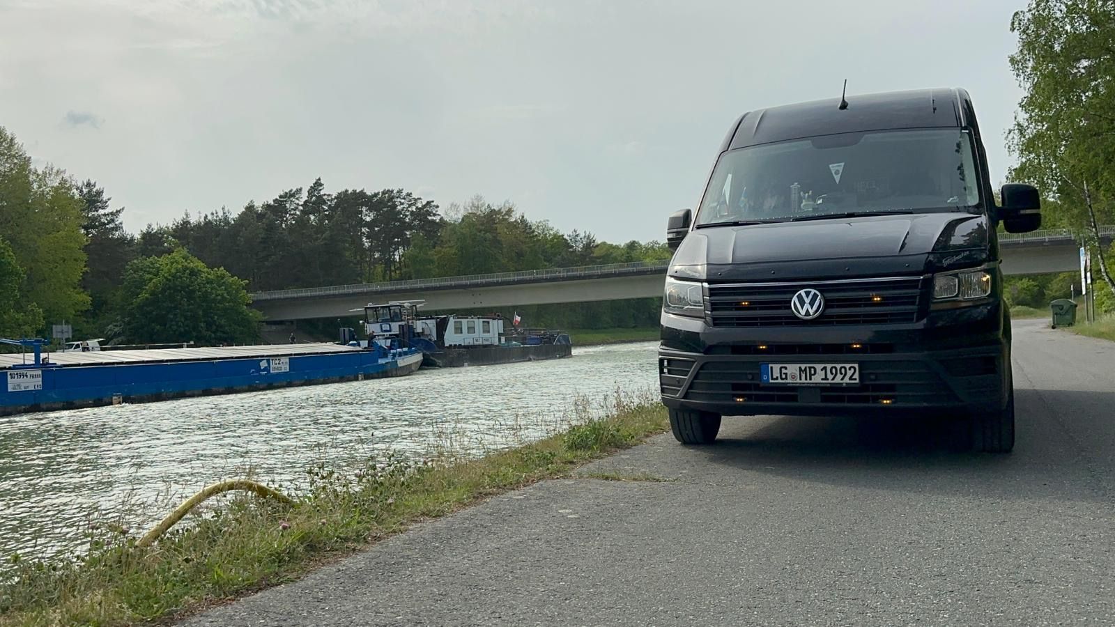Ein schwarzer Lieferwagen fährt eine Straße neben einem Gewässer entlang.