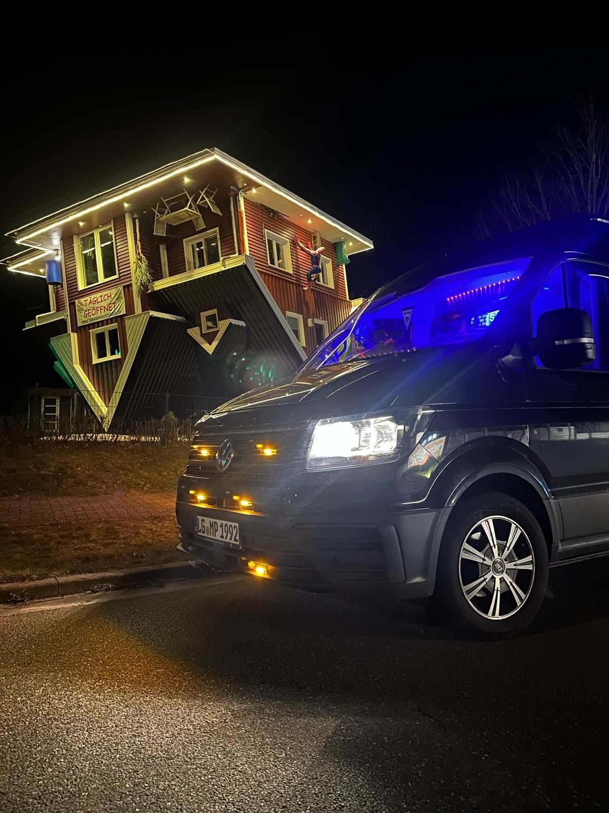 Nachts parkt ein Auto vor einem auf dem Kopf stehenden Haus.