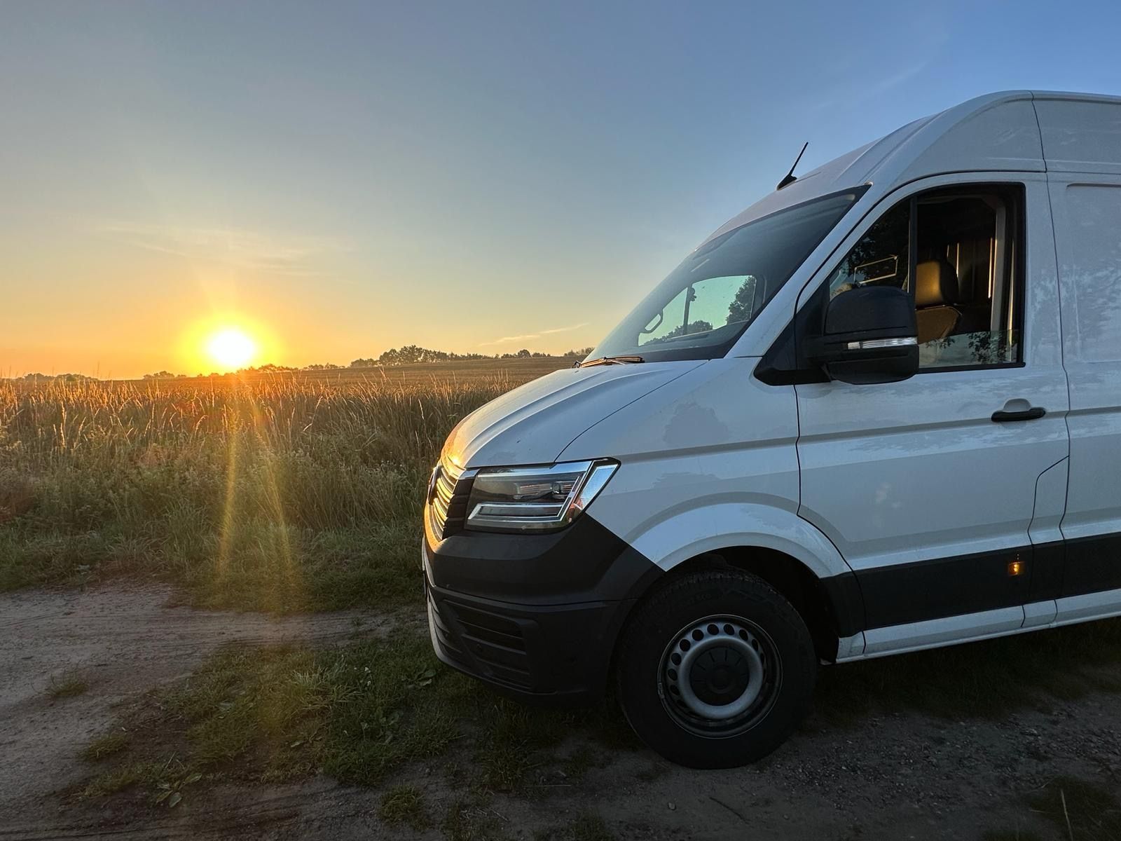 Ein weißer Lieferwagen parkt bei Sonnenuntergang auf einem Feld.