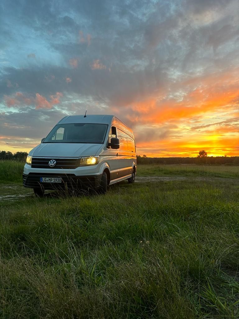 Ein weißer Lieferwagen parkt bei Sonnenuntergang auf einer Wiese.