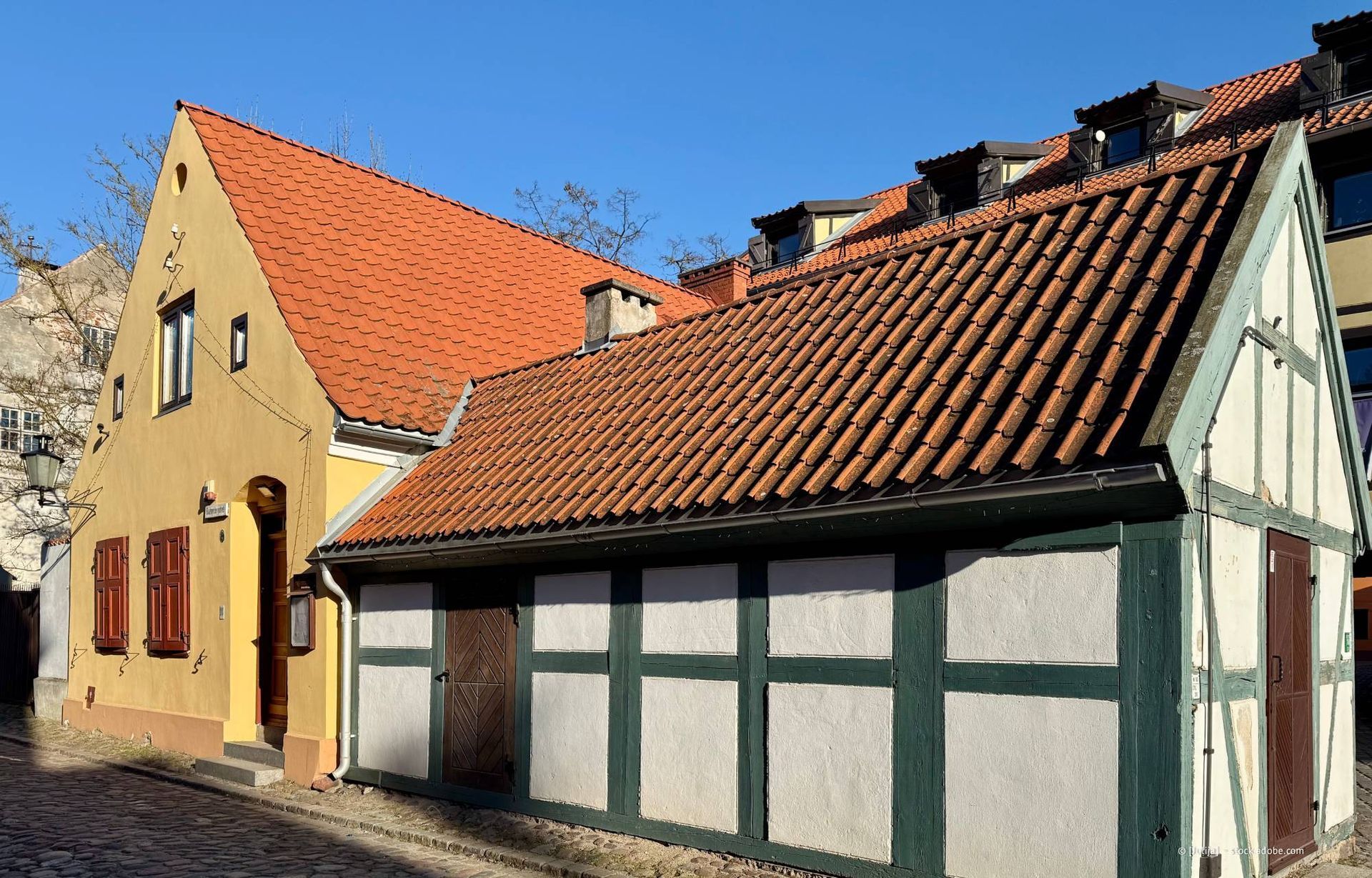 Gelbe und weiße Fachwerkhäuser mit roten Ziegeldächern vor einem klaren blauen Himmel.