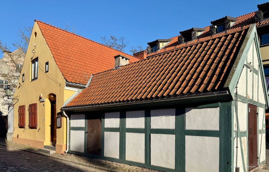 Gelbe und weiße Fachwerkhäuser mit roten Ziegeldächern vor einem klaren blauen Himmel.