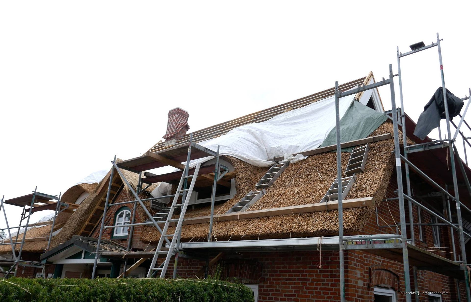 Das Reetdach eines Backsteinhauses wird repariert; Gerüste und Planen sind sichtbar.