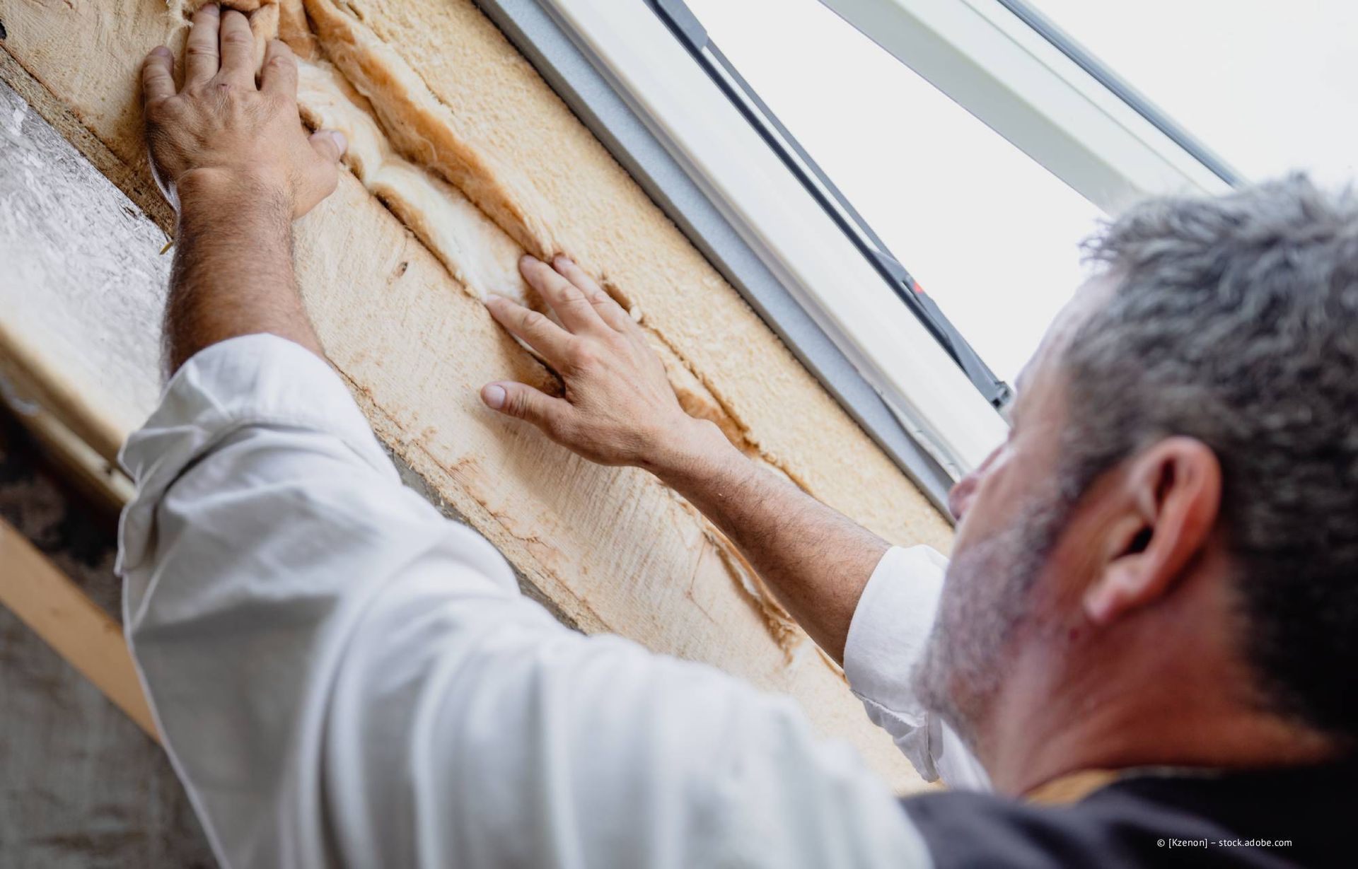 Eine Person isoliert einen Fensterrahmen mit einem faserigen Material.