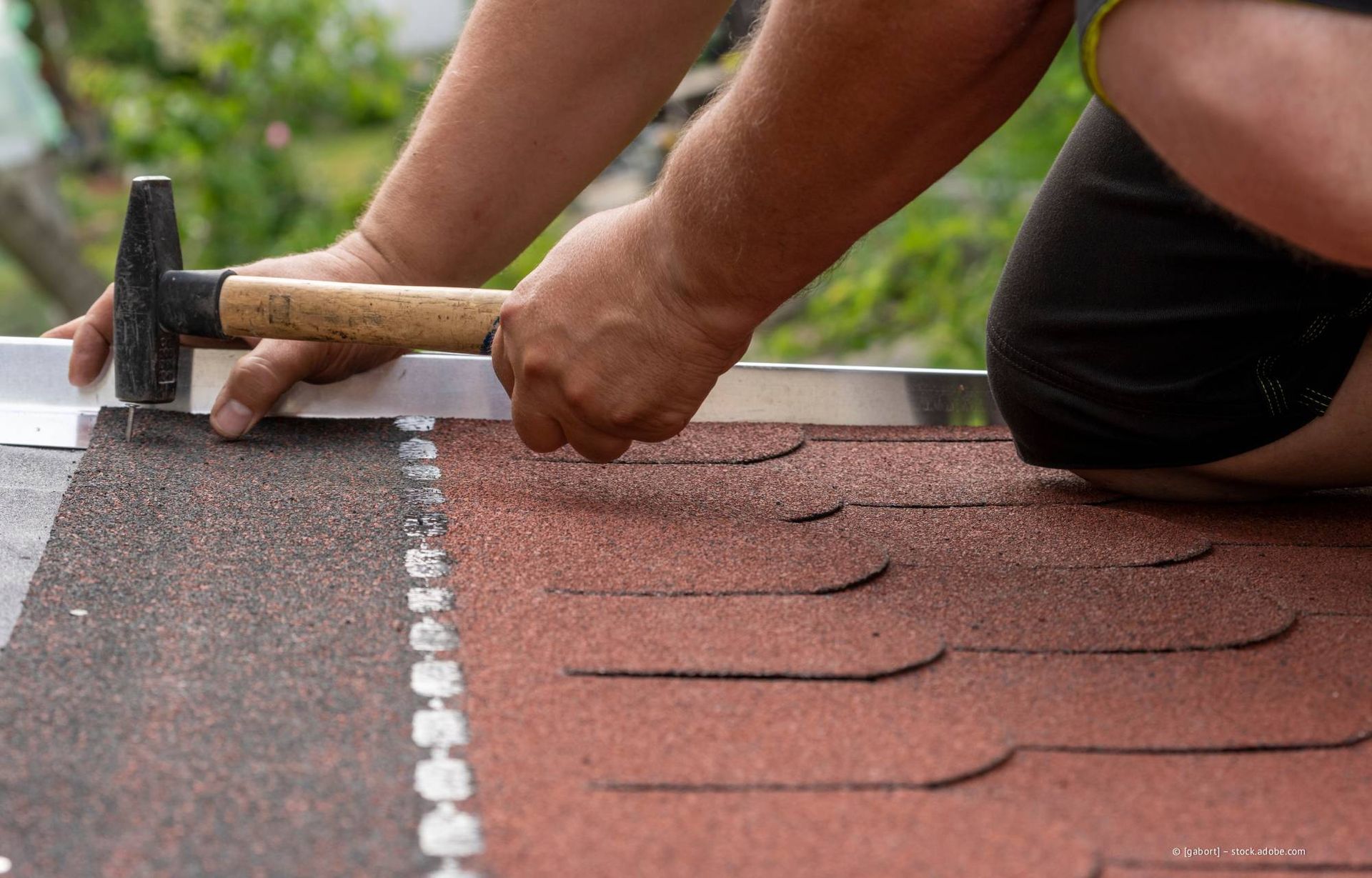 Eine Person schlägt mit einem Hammer eine Dachschindel auf ein Dach.