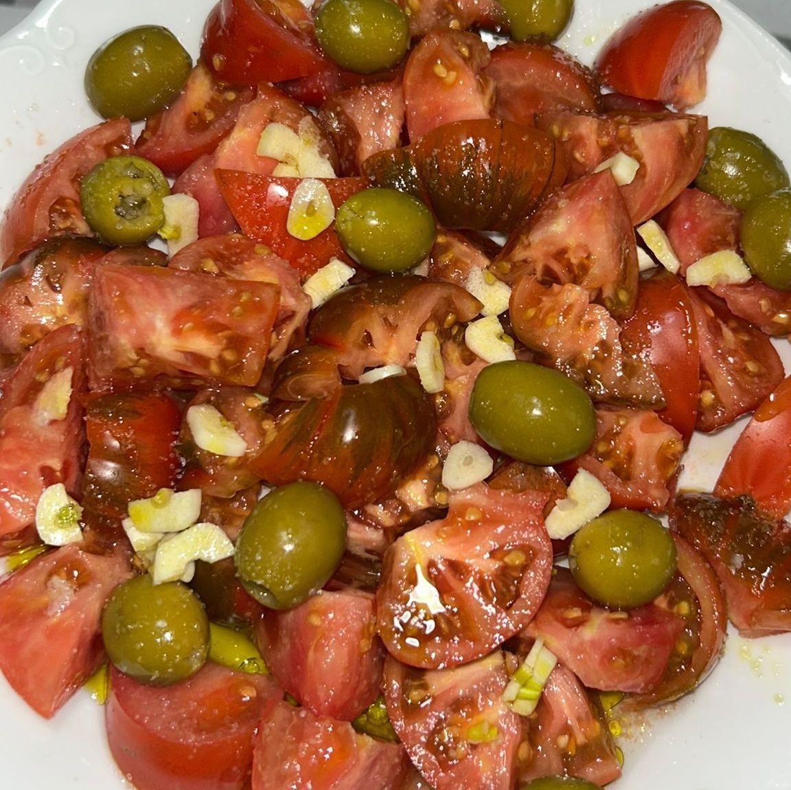 Tomates en rodajas, aceitunas verdes y ajo picado aliñados con aceite de oliva.