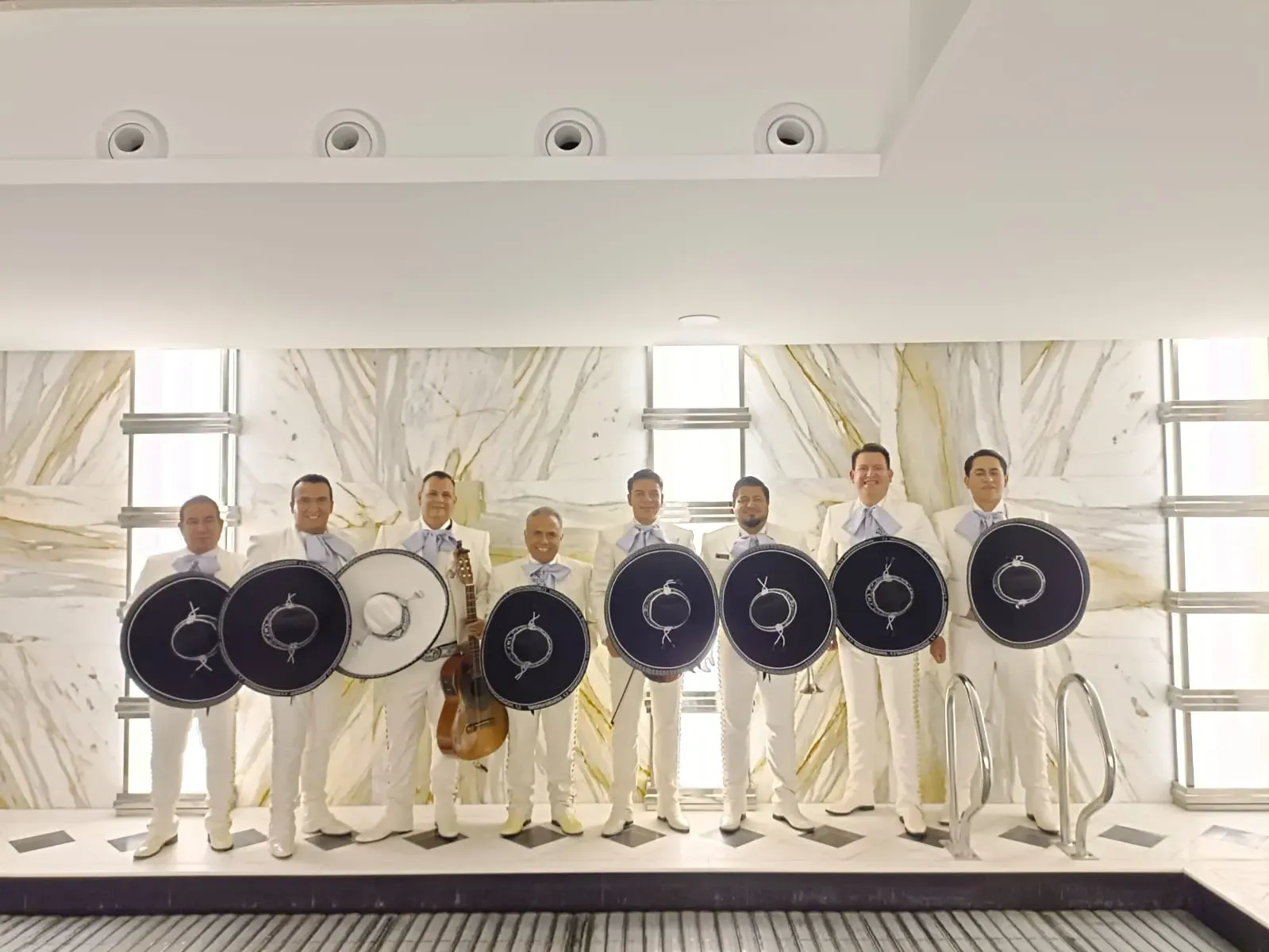 Ocho personas vestidas de blanco, sosteniendo escudos redondos