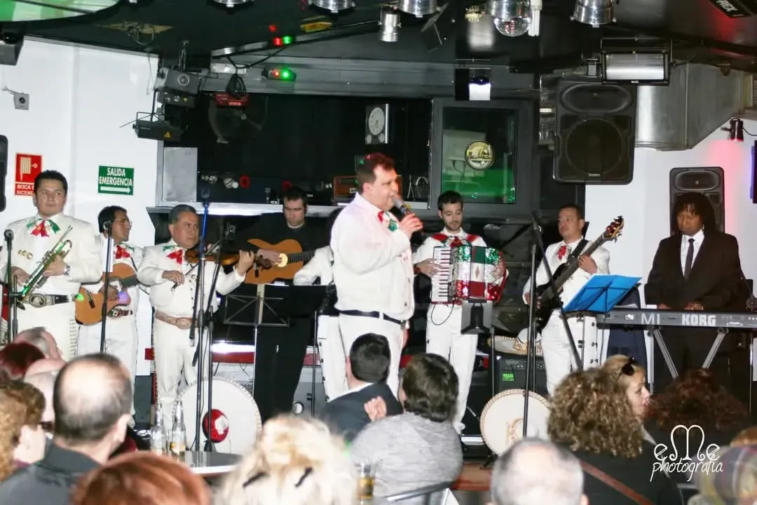 Un grupo musical actuando en un pequeño escenario interior, con un cantante en el centro y los instrumentos a su alrededor.