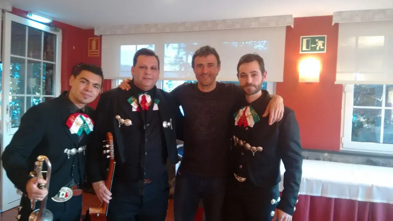 Cuatro hombres vestidos con atuendos oscuros y cintas rojas y blancas posan juntos en el interior de un evento.
