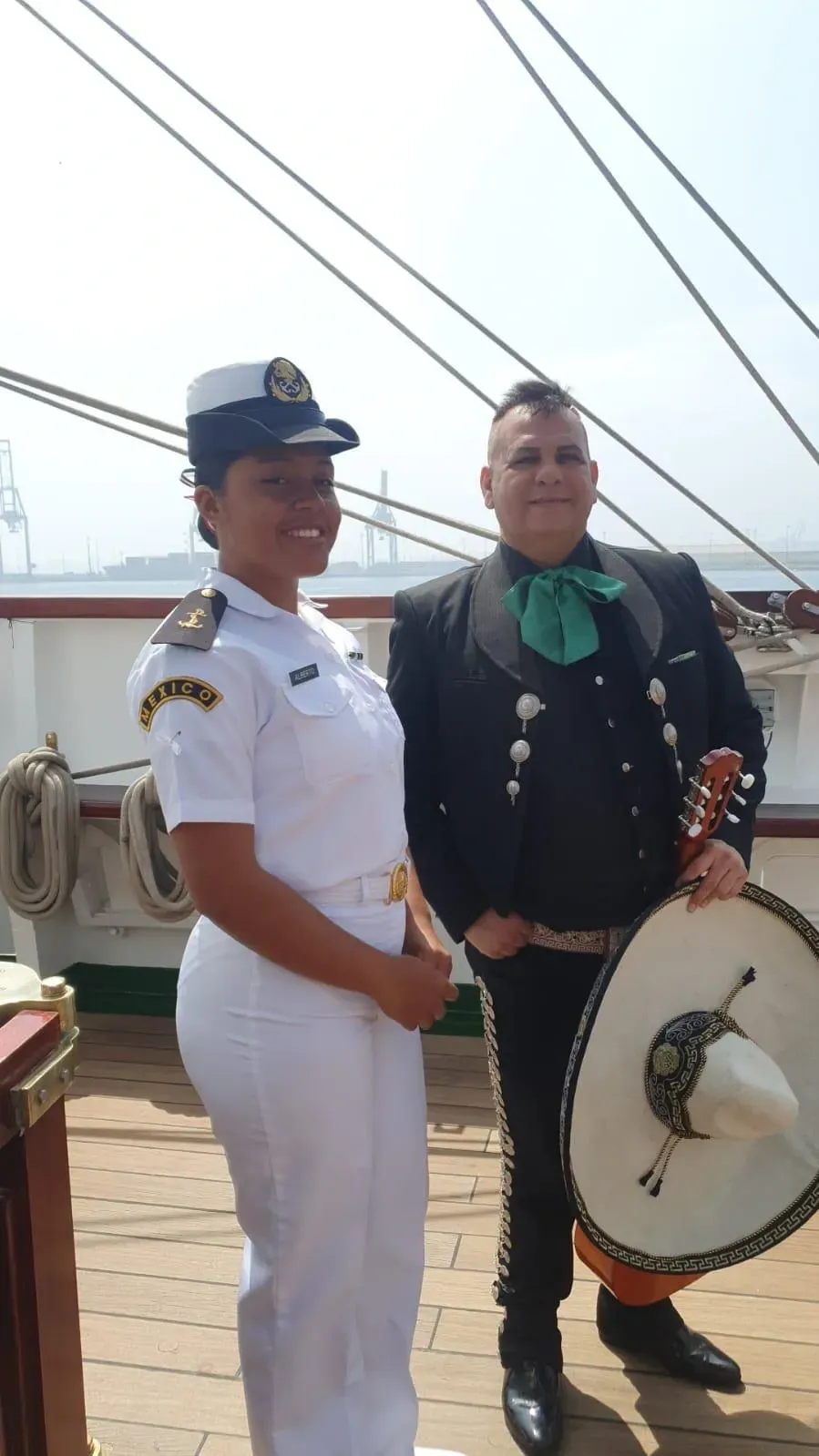 Dos personas vestidas con trajes de charro blancos y negros están de pie en la cubierta de un barco
