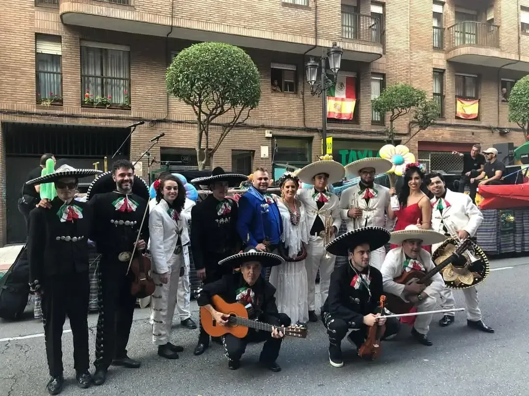 Grupo de mariachis actuando en un desfile callejero, con músicos vestidos con trajes blancos y negros y sombreros.
